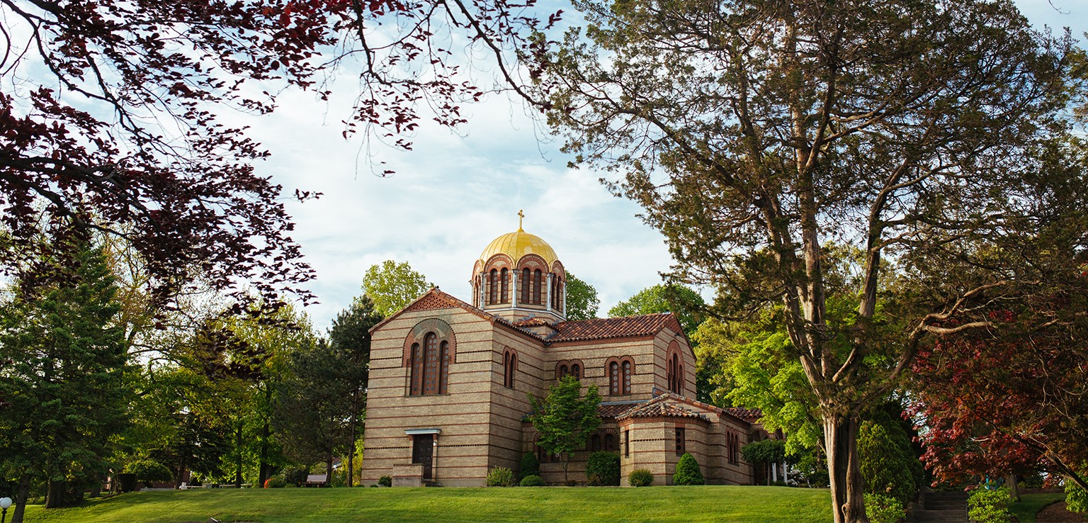 The orthodox church at Hellenic College Holy Cross topped with golden dome. Green lawn.